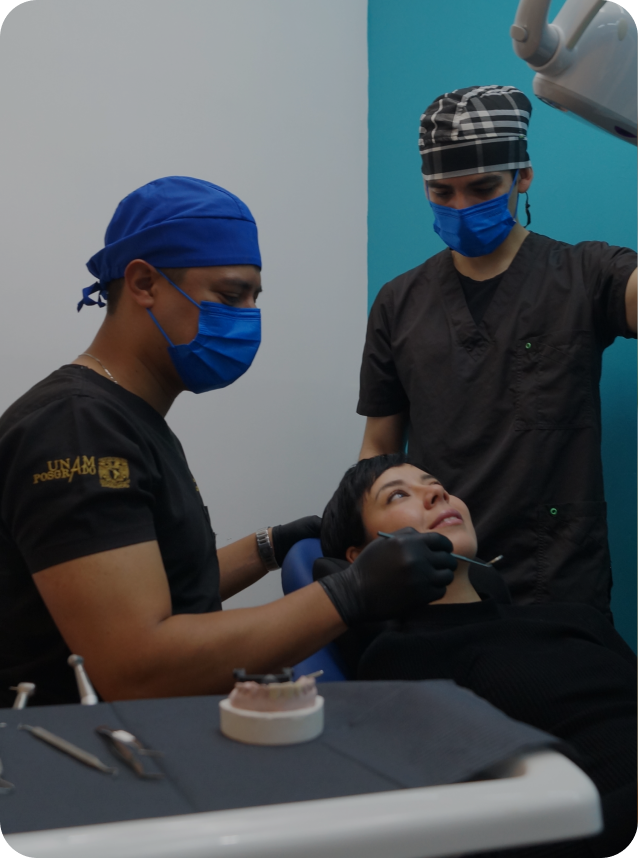 Paciente recostada en silla dental mientras dos dentistas con cubrebocas y guantes realizan una revisión.