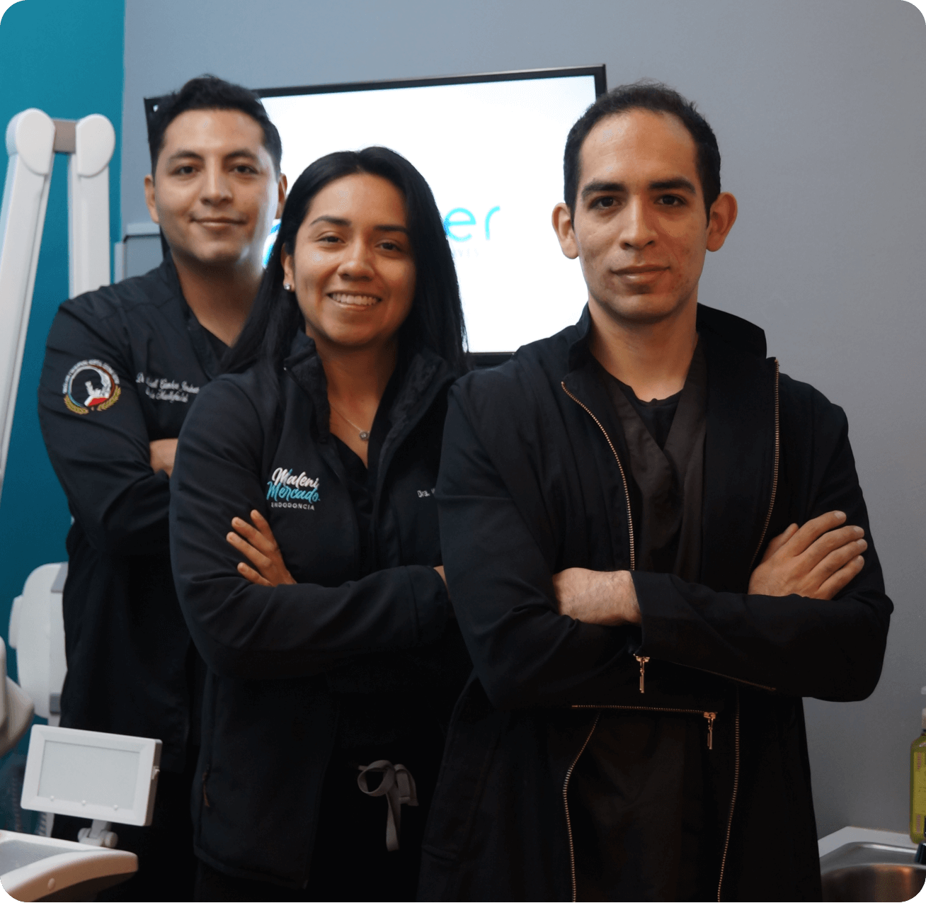 Tres profesionales de la salud dental con bata negra posan con los brazos cruzados en una clínica.